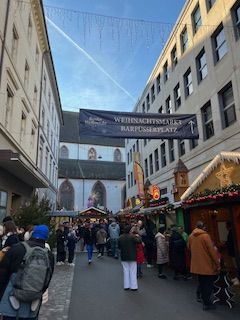 Christmas market on a street lined with stalls and buildings, people walking around, banner overhead.
