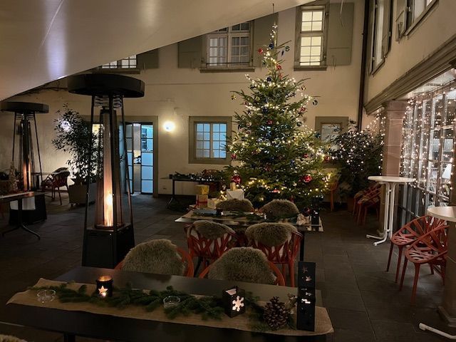 Outdoor patio decorated for Christmas with a lit tree, tables, chairs, and heaters.
