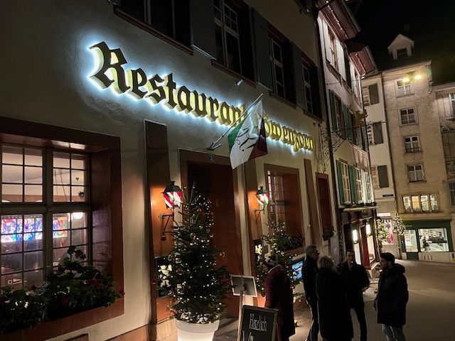 Restaurant exterior at night, lit sign, Italian flag, people outside.