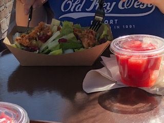 Salad and drink on a table; someone eats with a fork.