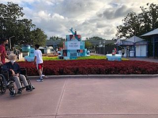 Person in wheelchair near a park display with a sign, surrounded by flowers.