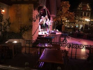 Band performing on a stage, with tables and chairs in front, near a building at night.