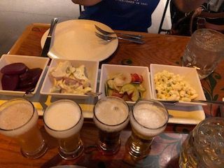 Beer flight with four small glasses and four side dishes on a wooden table.