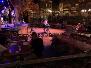 Live band performing on stage in a restaurant. People sit at tables, watching and eating.