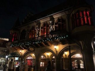 Night view of a building with arches and statues. Red-lit windows, festive garland.