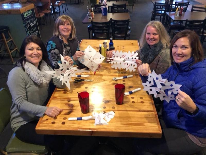 A group of women are sitting at a table holding paper snowflakes.