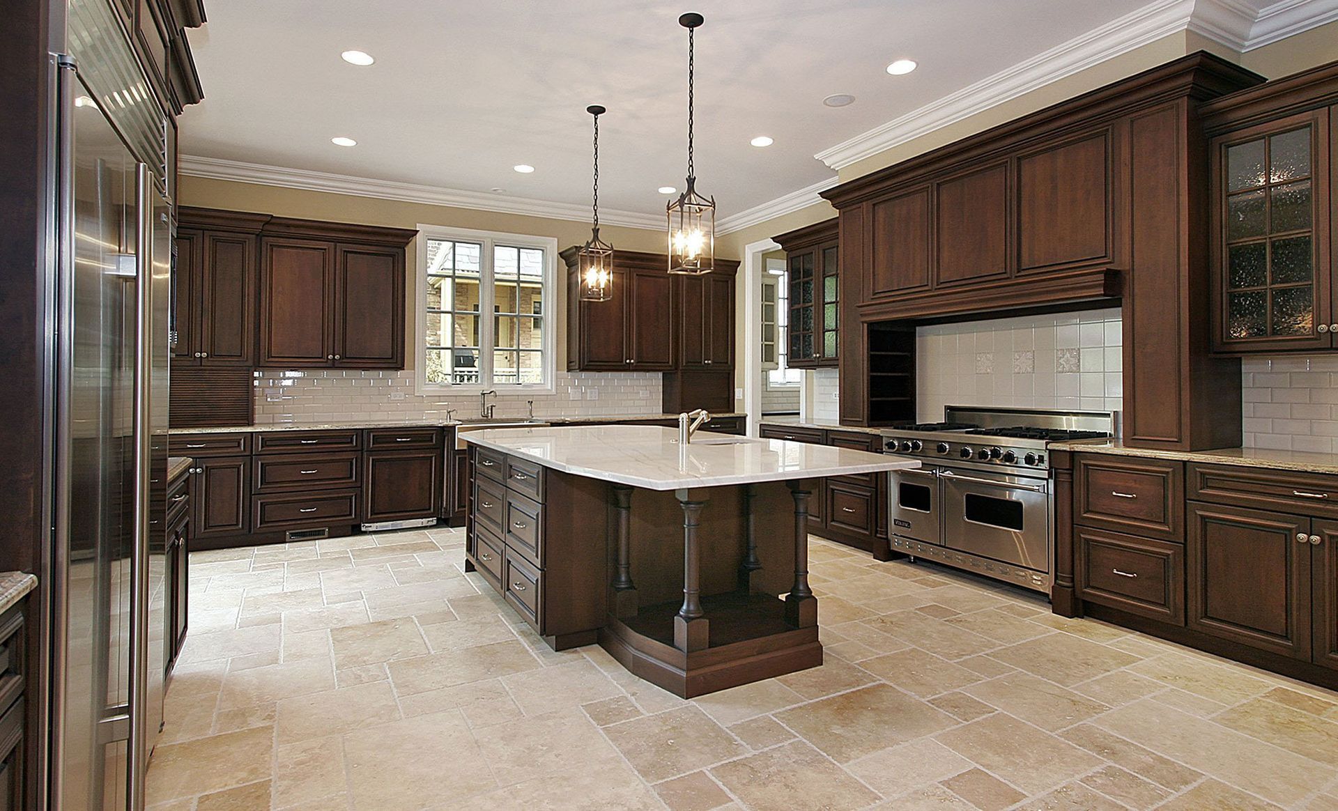 Elegant kitchen with dark wood cabinets, large island, stainless steel appliances, and stone floor.