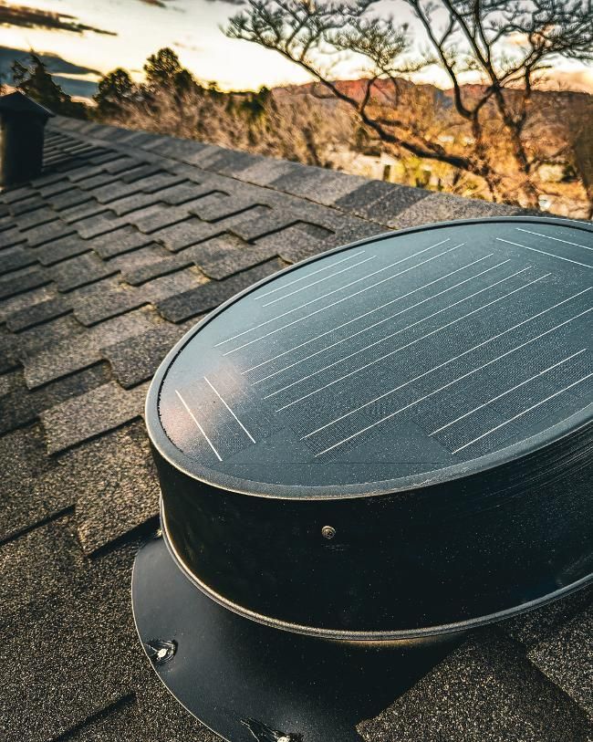 Solar-powered roof vent on a shingled roof with a mountain view in the background.