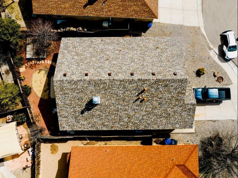 Overhead view of a house with a brown roof, parked cars in the driveway, and surrounding homes.