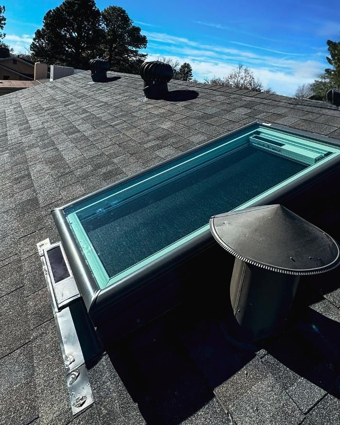 Skylight and vent on a shingled roof under a bright blue sky.