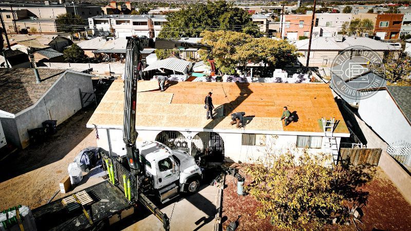 Roofing crew replacing a roof on a residential home. Crane lifts materials, workers on the roof.