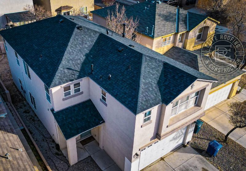 High-angle view of a two-story house with a dark shingle roof. Beige siding, white trim, and a concrete driveway.