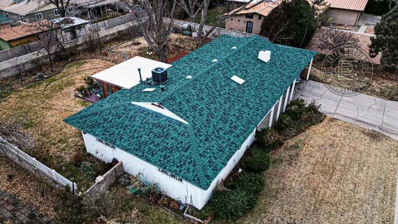 Aerial view of a white house with green roof in a yard with sparse vegetation and a driveway.