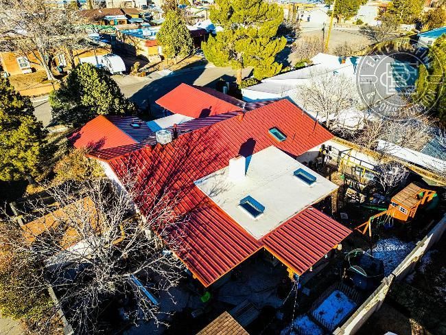 Aerial view of a red-roofed house with skylights, surrounded by trees and other buildings.