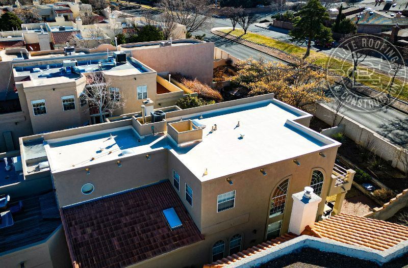 Overhead view of stucco buildings with flat white roofs and a red-tile roof section in a suburban area.