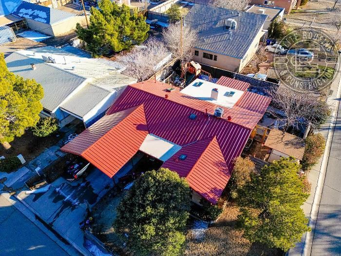 Aerial view of a house with a red roof, trees, and surrounding houses on a sunny day.