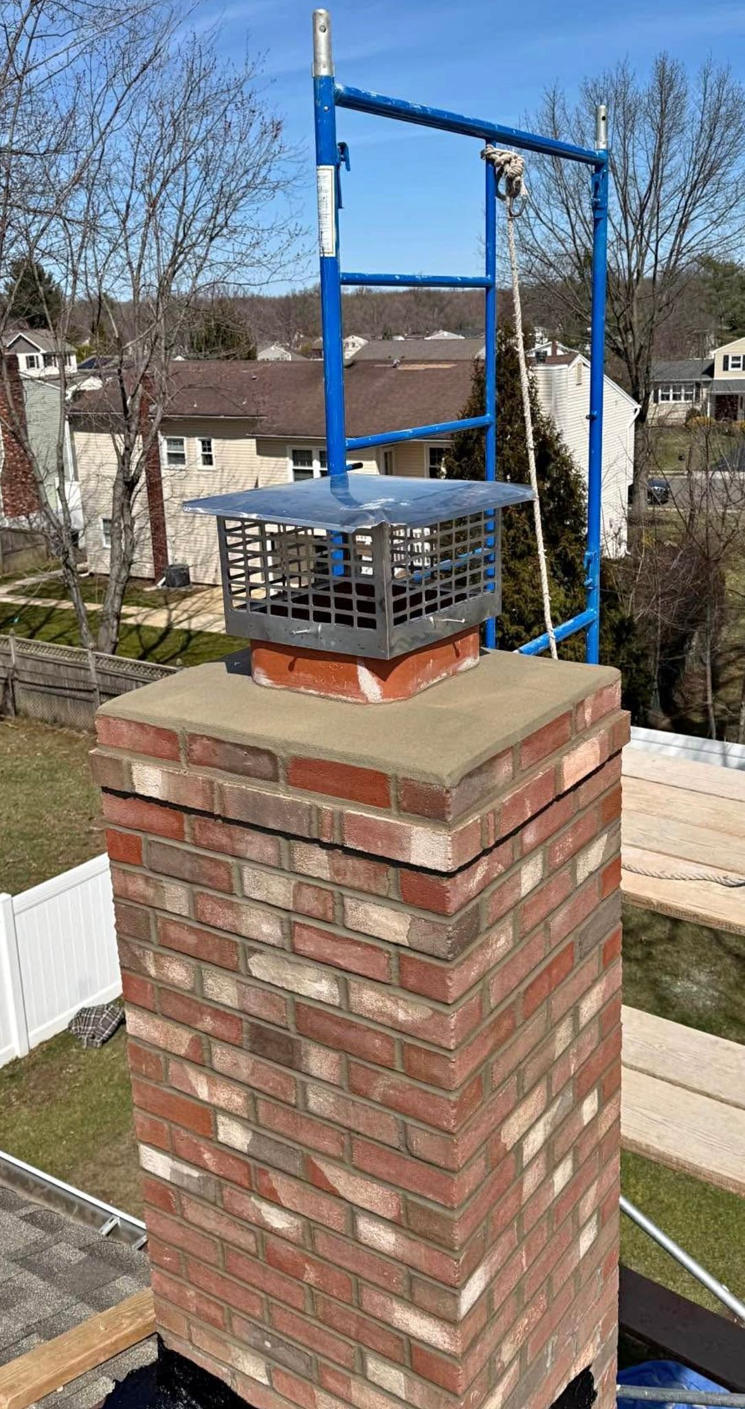 Brick chimney with a metal cap and blue scaffolding on a rooftop.