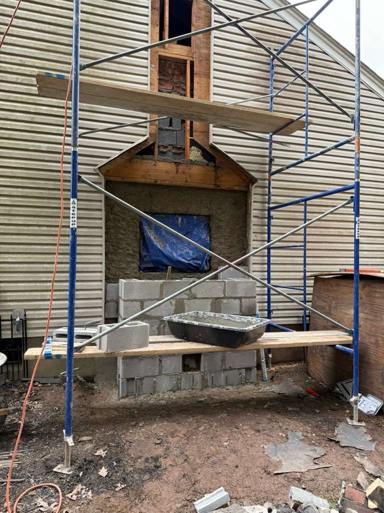Chimney construction on house exterior, using scaffolding. Grey cinder blocks and mortar visible.