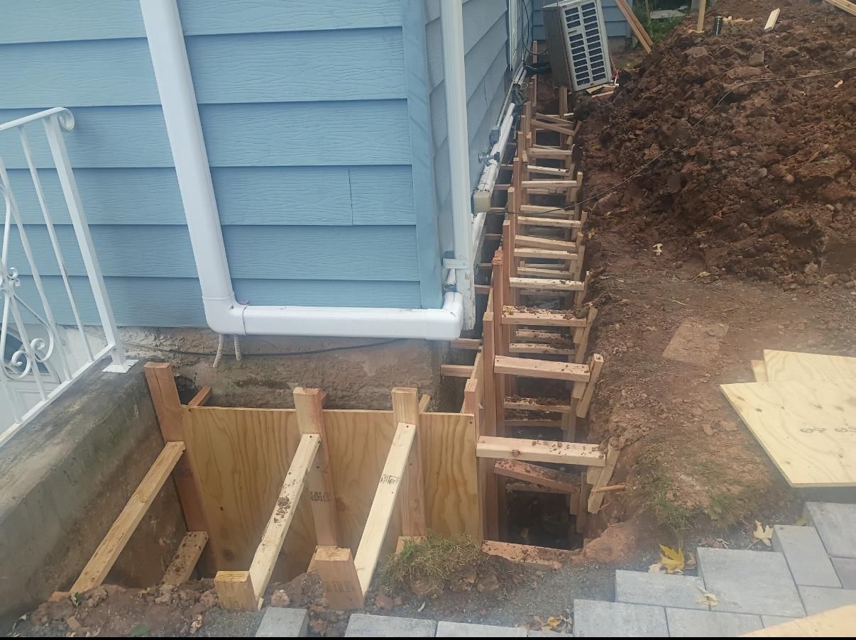 Construction site: wooden forms next to a blue house, ready for concrete work.