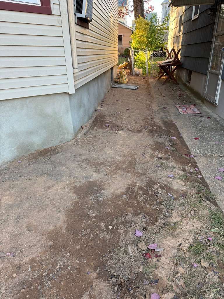 A narrow, dirt pathway between two buildings. The ground is uneven with scattered debris.