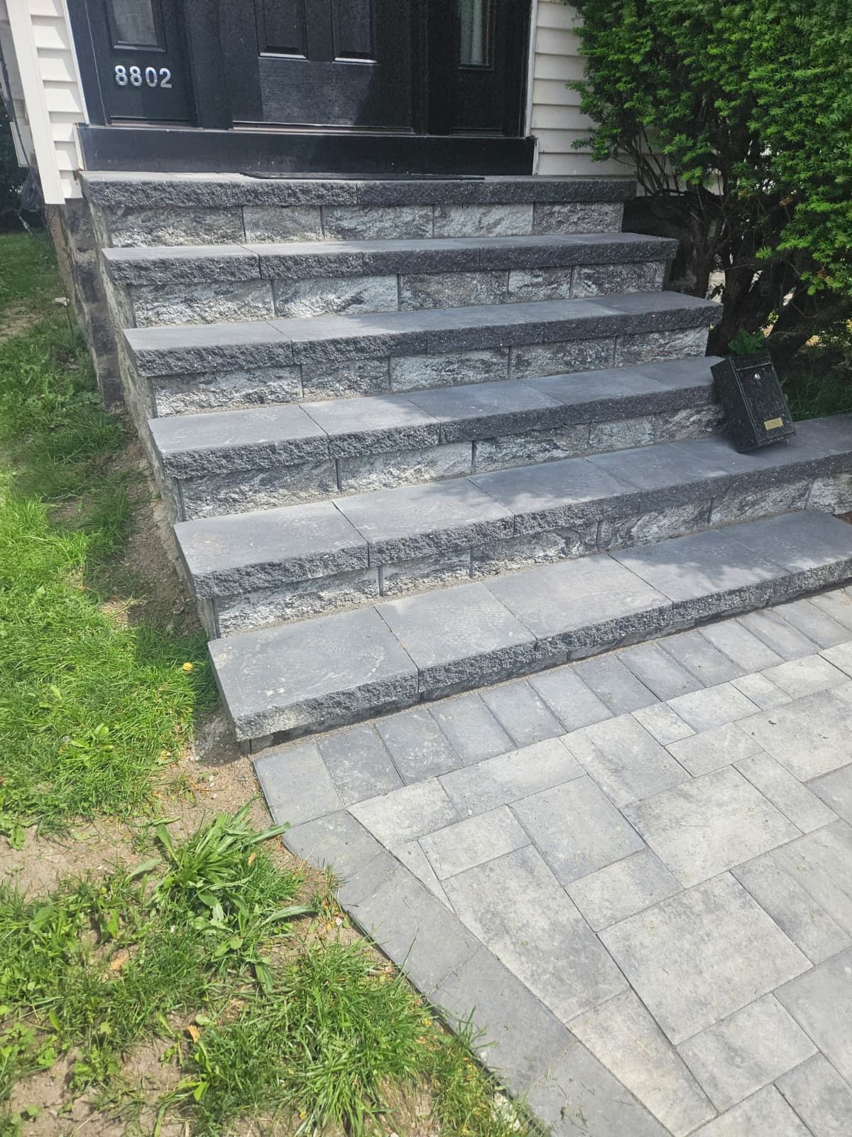 Grey stone steps leading to a dark doorway, bordered by green grass and a paved pathway.