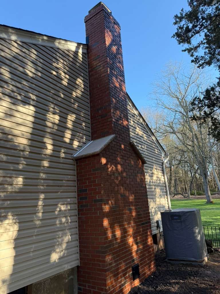 Brick chimney attached to a light brown house with an air conditioning unit outside.
