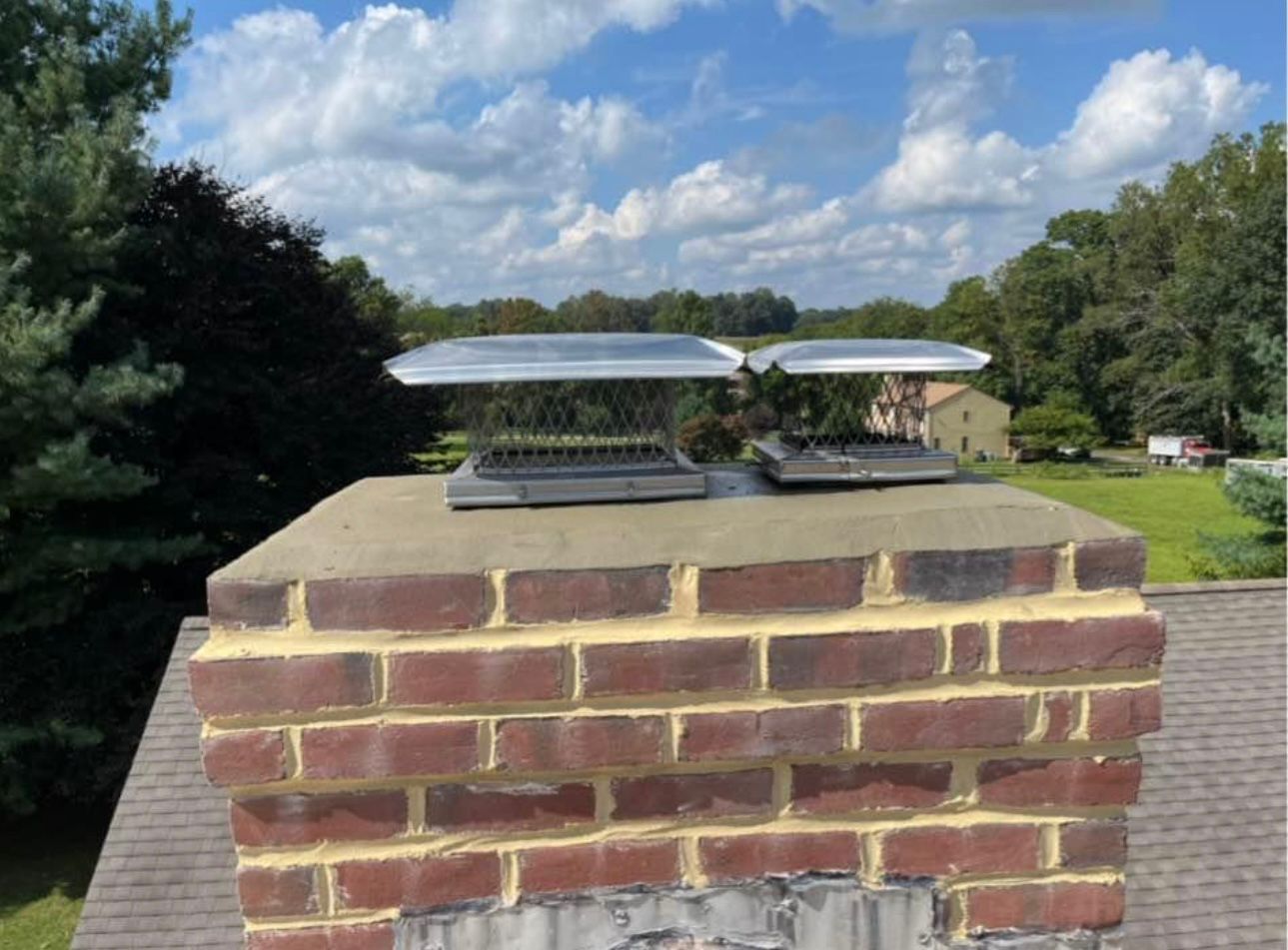 Brick chimney with two chimney caps against a blue sky with trees.