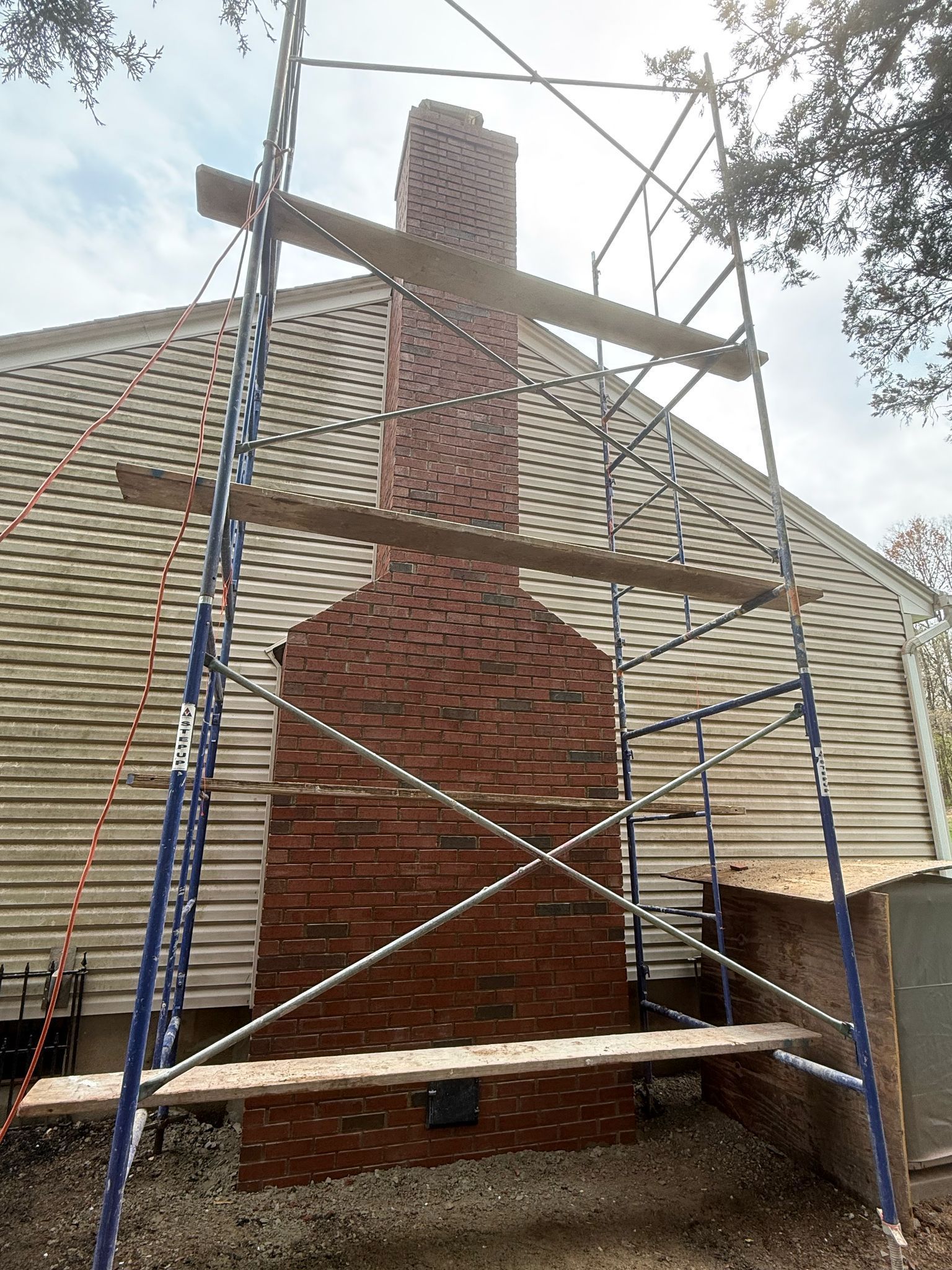 Brick chimney with scaffolding against a house, sunlight overhead.