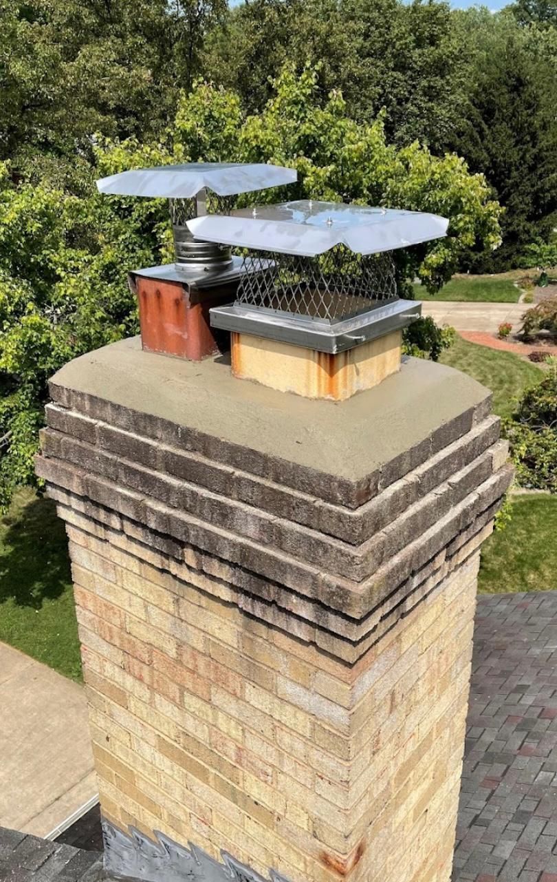 Chimney with multiple chimney caps against a backdrop of trees and a green lawn.