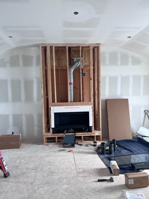 A living room under construction with a fireplace in the middle.