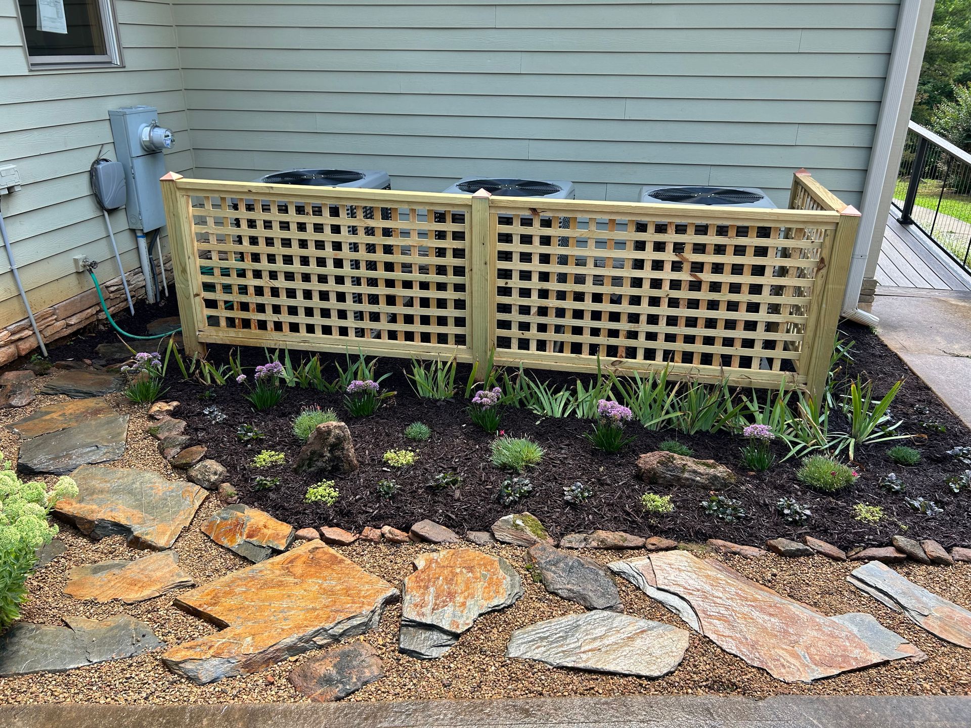 Two lattice compost bins beside a house wall, with a stone path and small garden bed in front