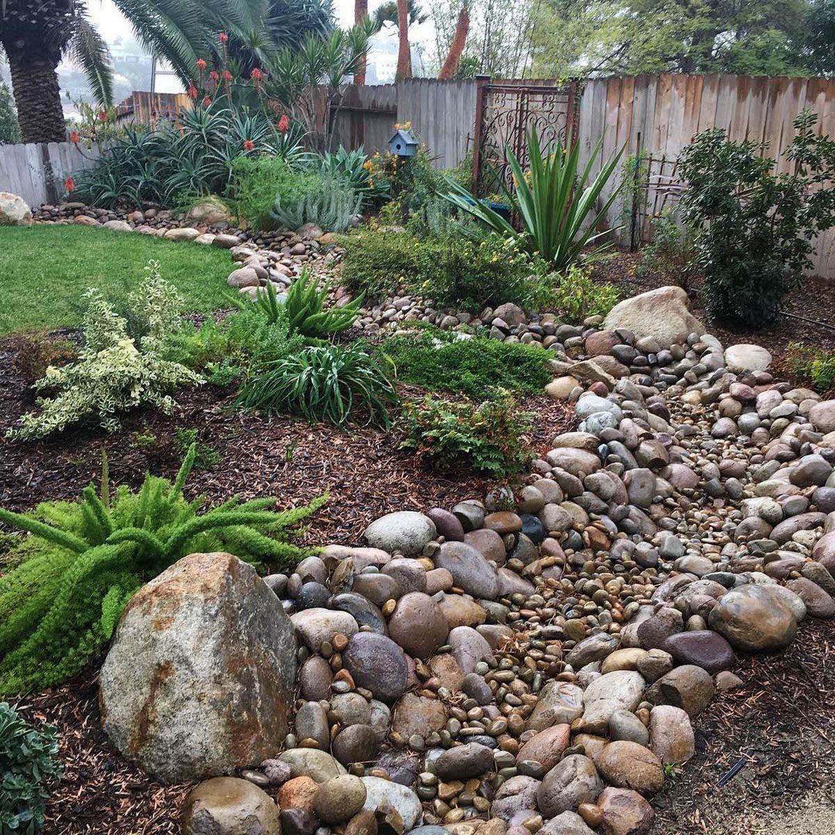 Rock garden with rounded stones, succulents, and a wooden fence in a landscaped backyard