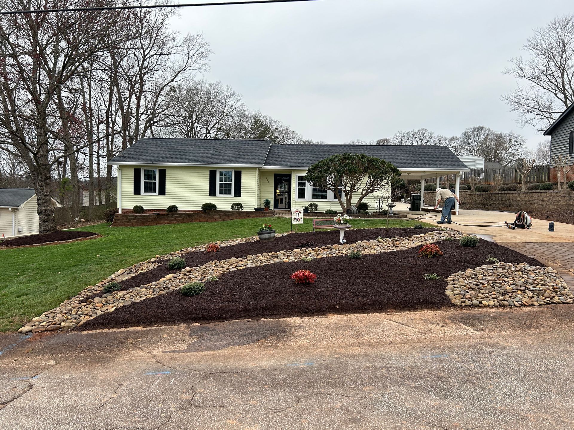 Single-story yellow house with a landscaped front yard and stone-edged garden beds