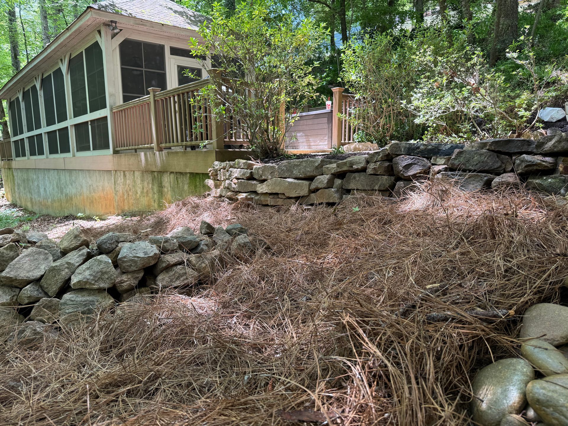 Wooded riverside with stone retaining walls and a screened porch beside a calm waterway