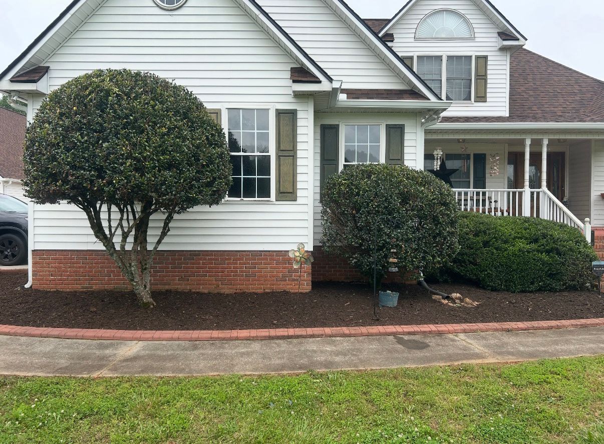 Suburban house exterior with white siding, brick foundation, trimmed bushes, and a front porch