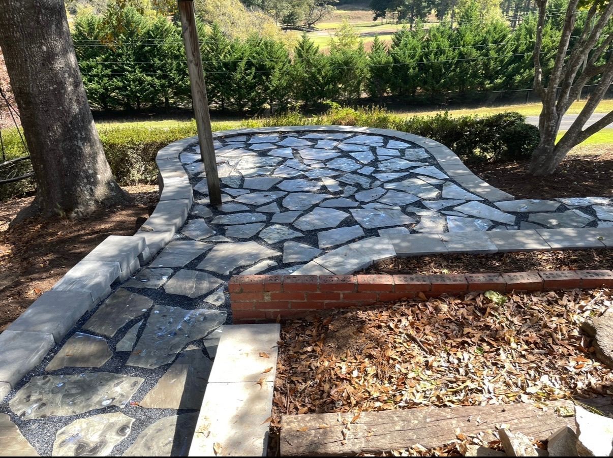 Stone garden path beside a wooden border and mulch, with trees and shrubs in the background