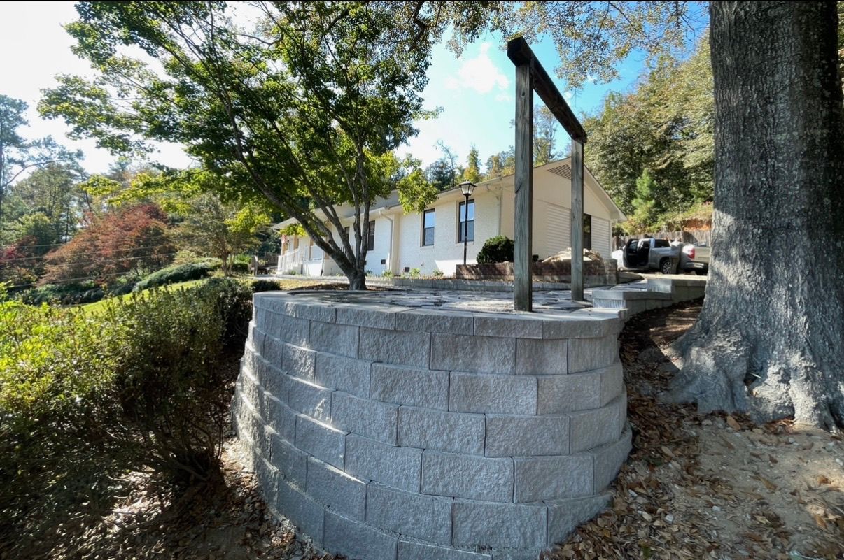 Stone retaining wall with black metal railing beside a tree-lined sidewalk and white building