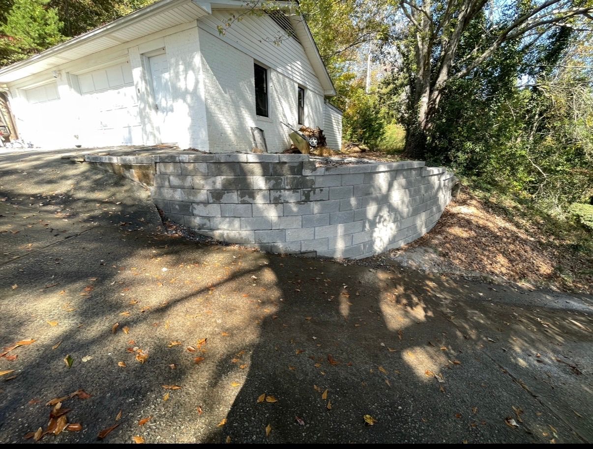 White building with a raised concrete patio beside a wooded driveway in bright sunlight