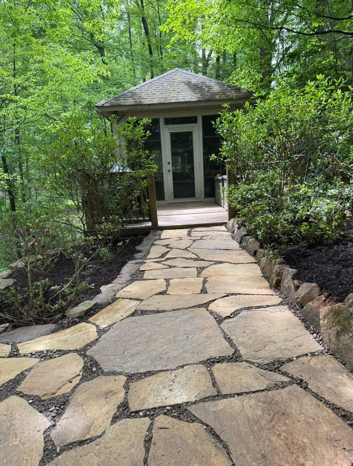 Stone path leading to a small garden pavilion surrounded by greenery