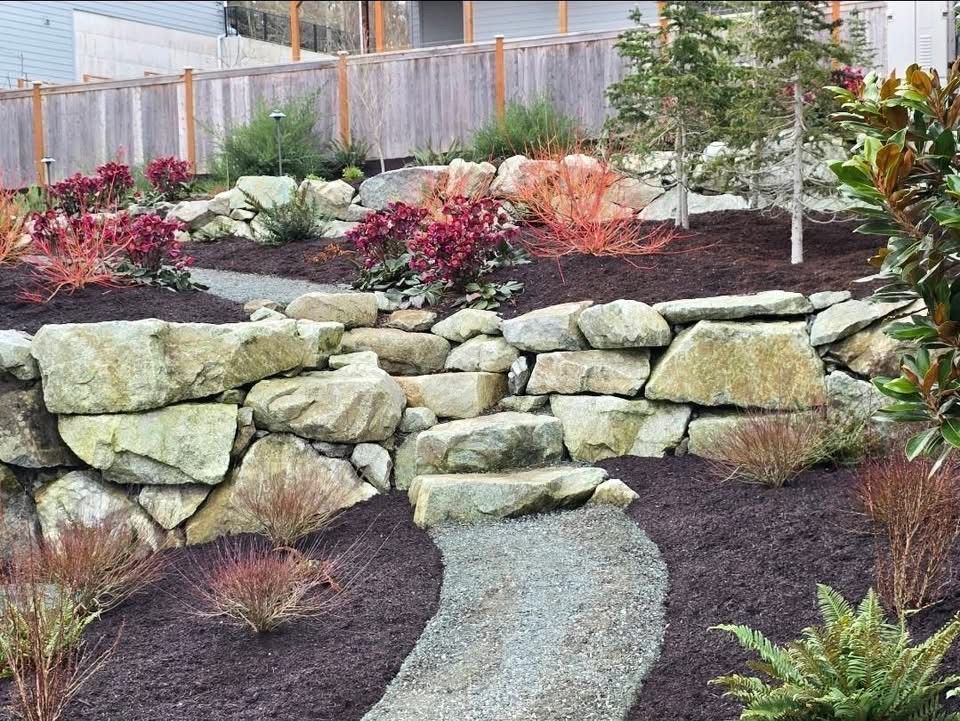 Landscaped garden with stone retaining wall, curved path, and red and green shrubs