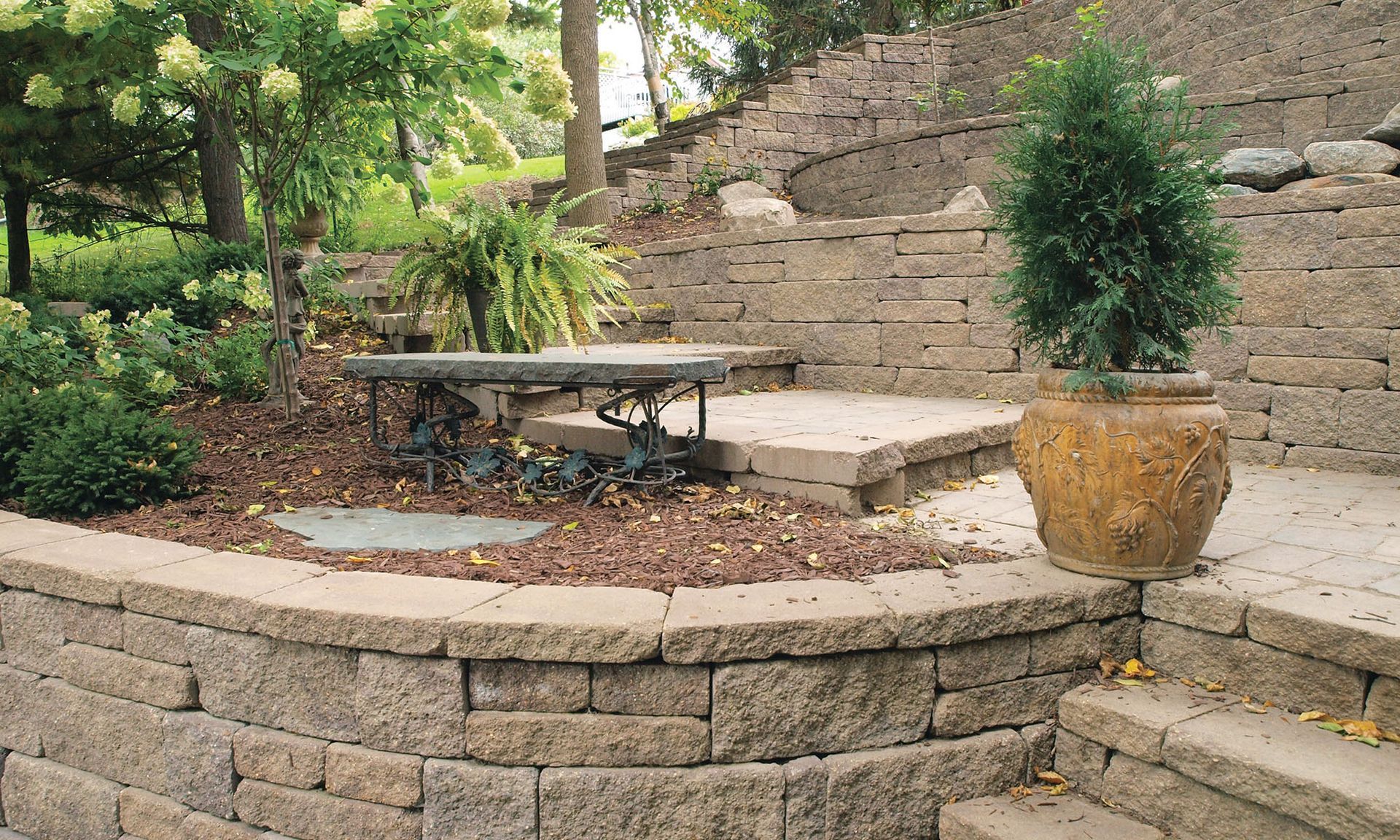 Terraced stone patio with bench, potted plant, and steps in a landscaped garden