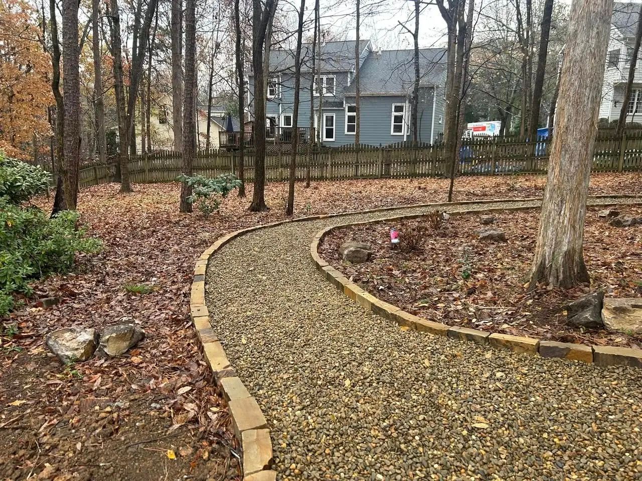 Curved gravel path through a wooded yard leading to a gray house in autumn