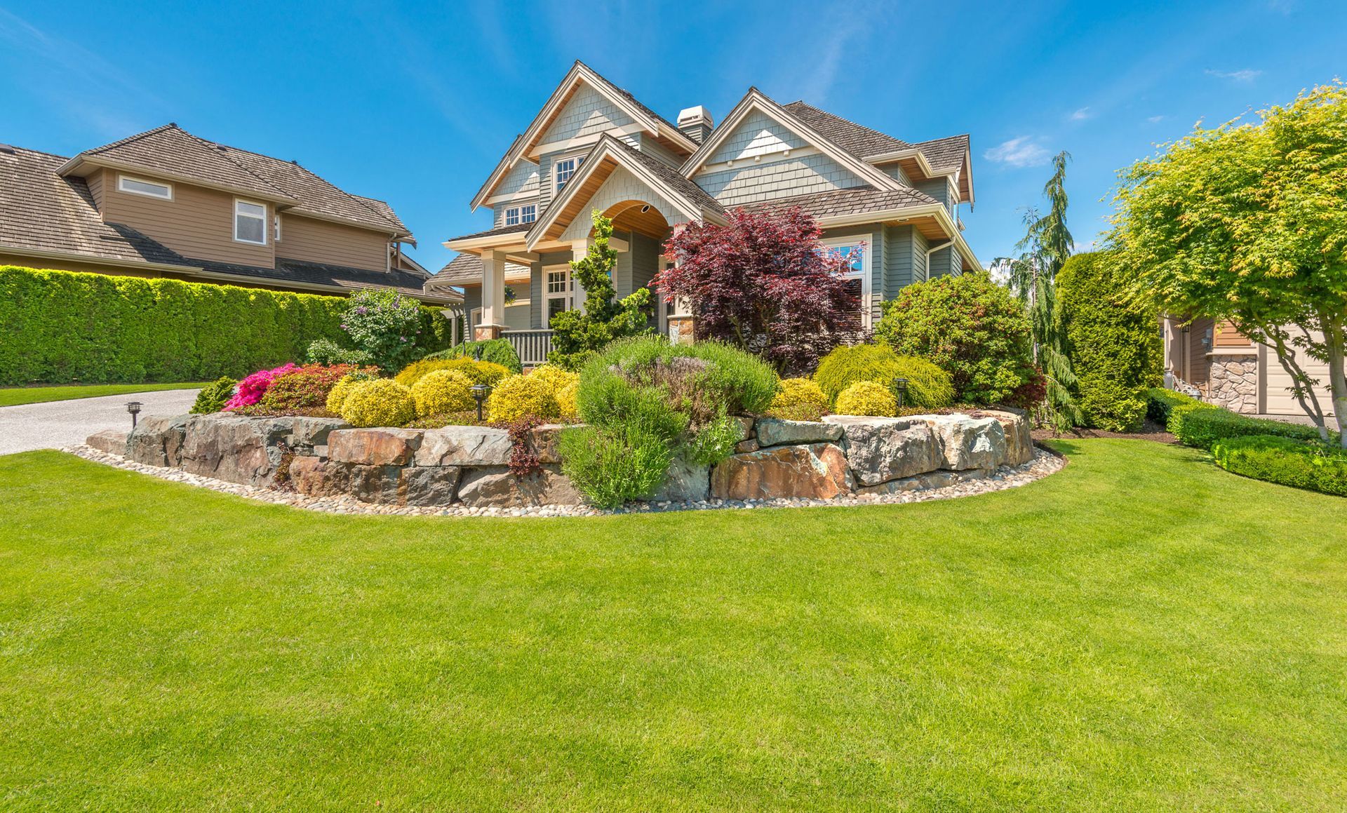 House with vibrant landscaping and lush green lawn under a bright blue sky.