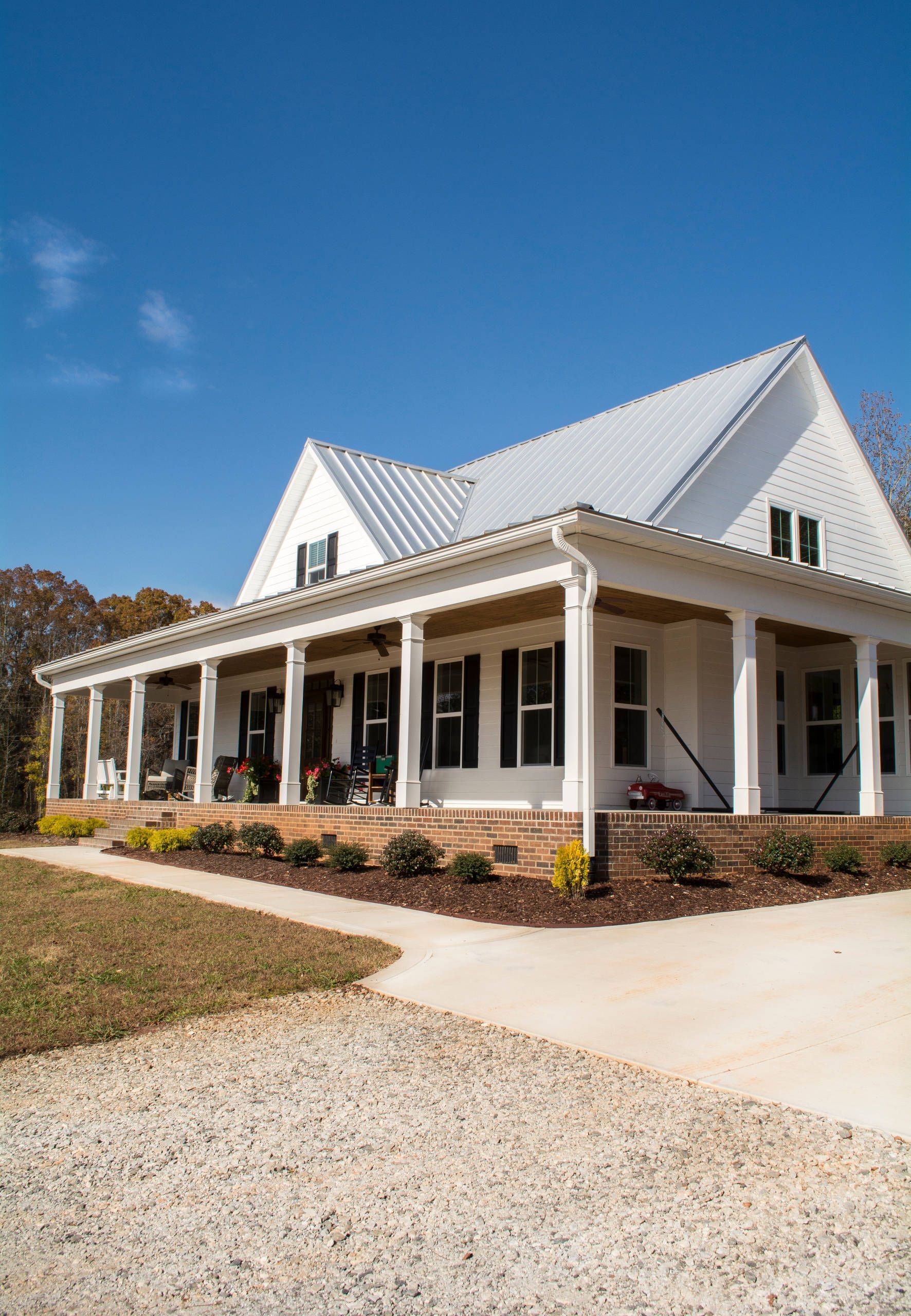 White house with wraparound porch and steep metal roof on a sunny day