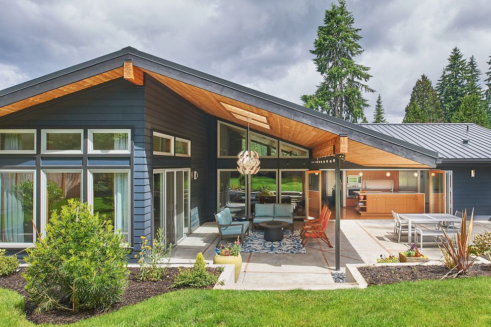 Modern house with large windows, covered patio, and outdoor seating in a landscaped yard