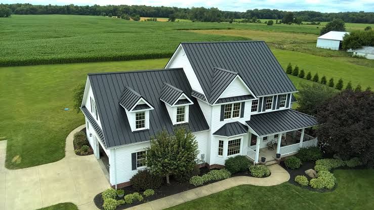 Large white two-story house with dark roof on a green lawn beside open farmland