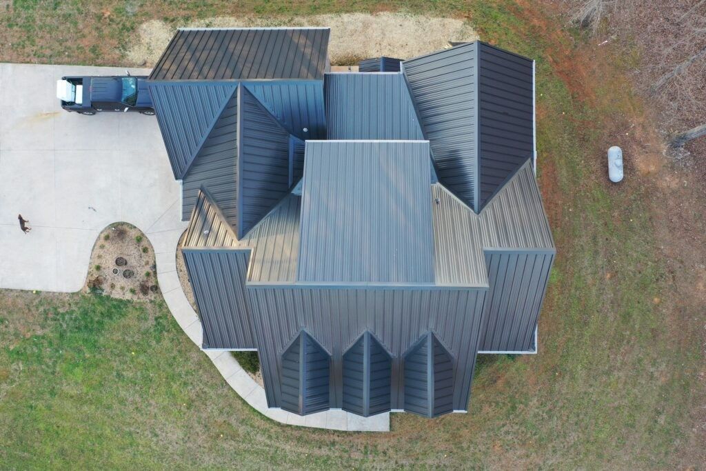 Aerial view of a large gray-roofed house with a driveway and grassy yard.