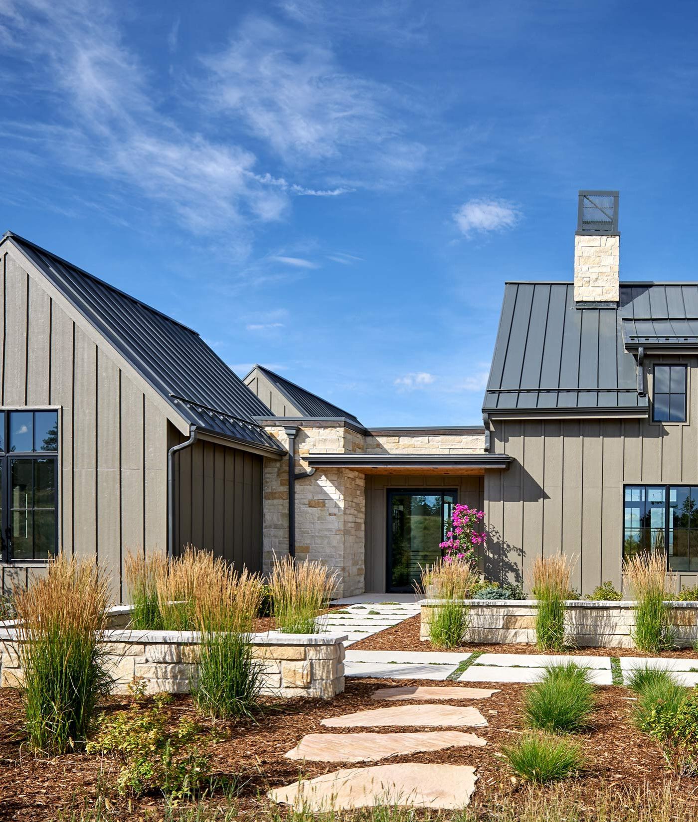 Modern gray house with metal roofs, stone path, and landscaped garden under a blue sky
