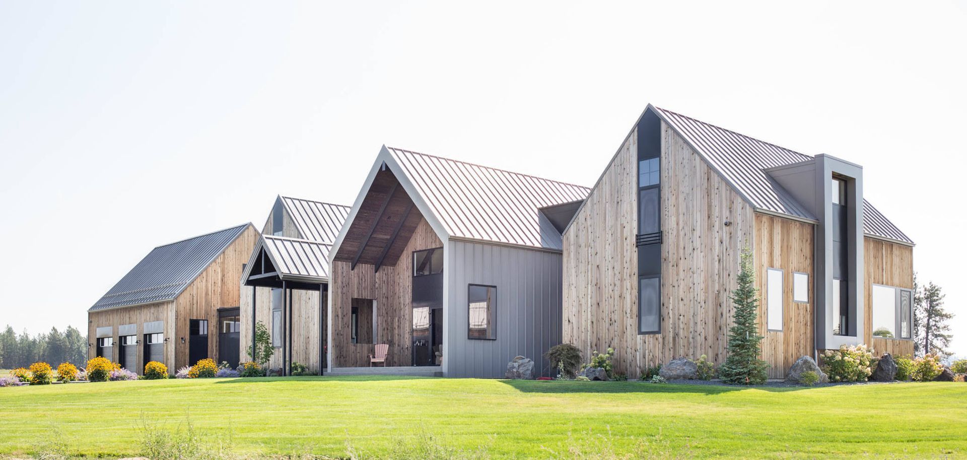 Modern gray-and-wood houses with metal roofs on a sunny green lawn