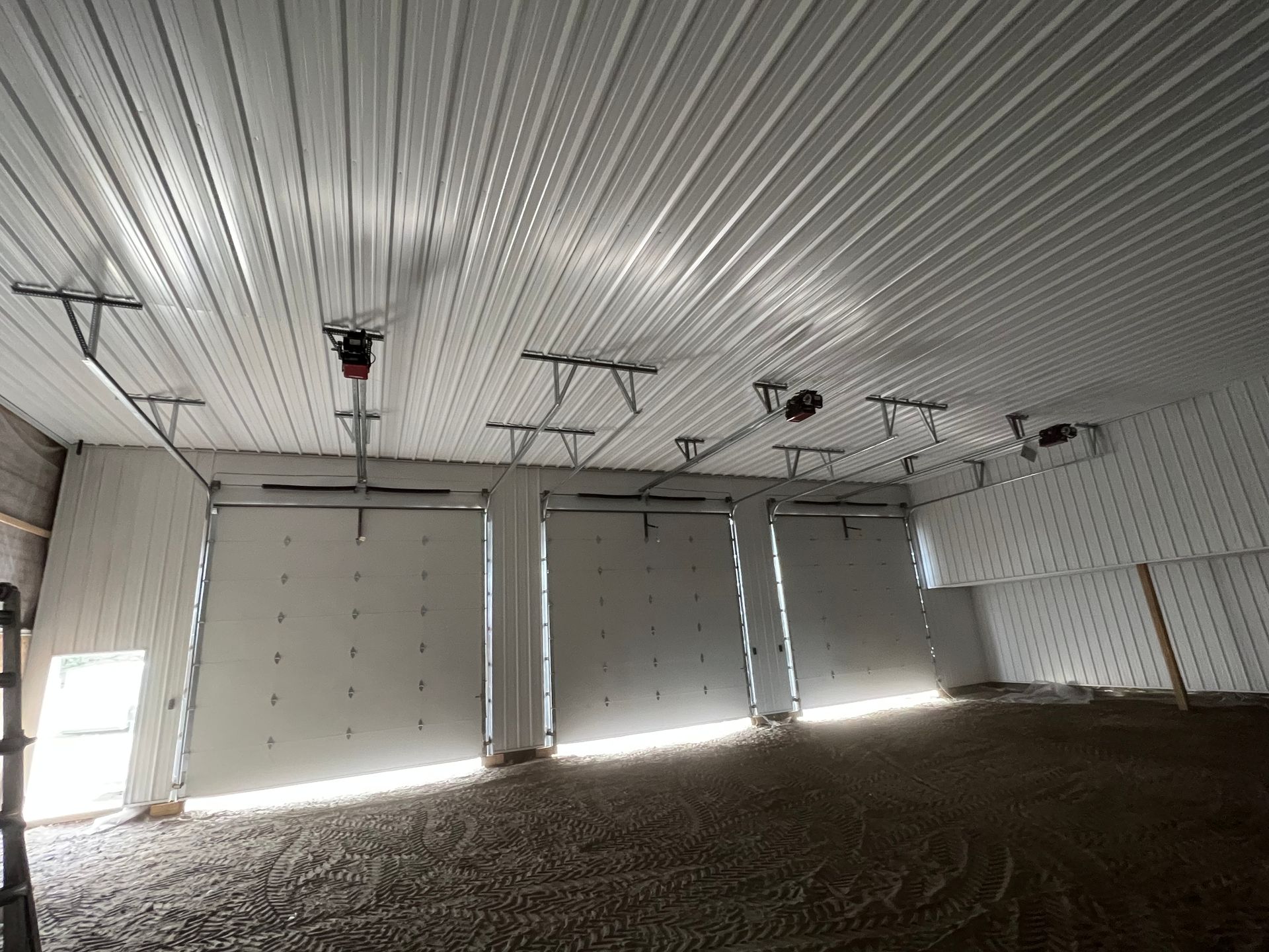Empty industrial garage with white metal ceiling and closed doors, bright light streaming through gaps.